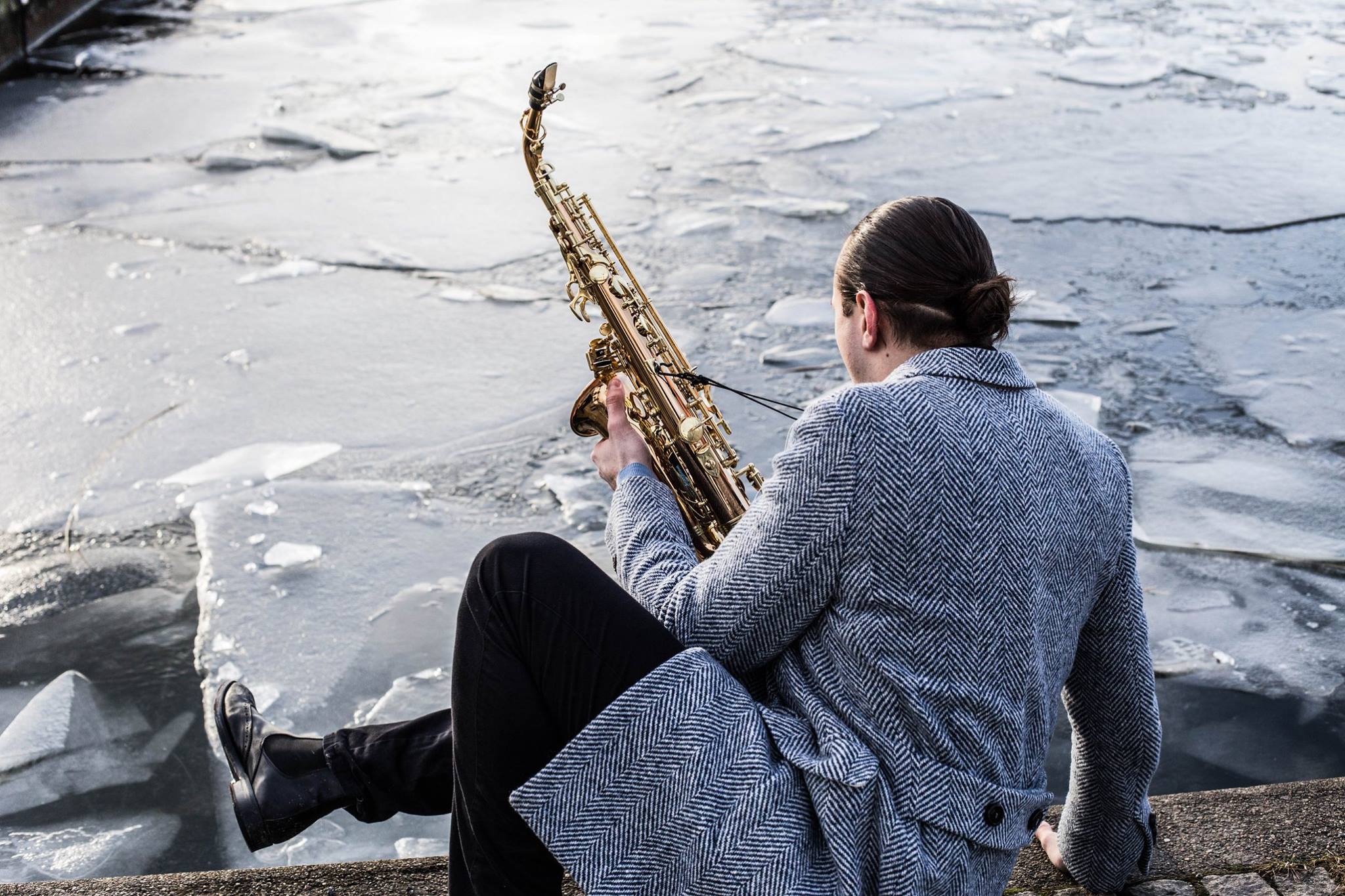 Andreas Ferronato sitter vid en islagd sjö med sin saxofon